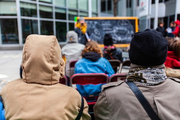 Audience watch environment demonstration. Attendees are viewed from behind, wearing warm clothes as the brave the bad weather to watch a presentation held by eco-activists in the city.