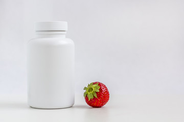 White medicine bottle for pill or vitamin dietary supplement and strawberry on white background.