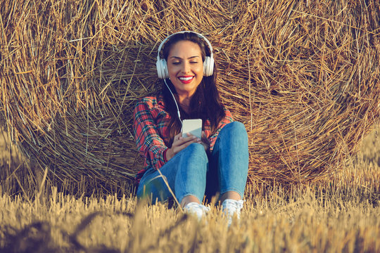 Girl sitting in the wheat field with her headset on. She is leaning her back on a haystack.