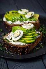 Avocado sandwich on dark rye bread made with fresh sliced avocado, eggs, cream cheese. black wood background