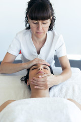 Masseur doing therapeutic face massage to young pregnant woman in spa center.