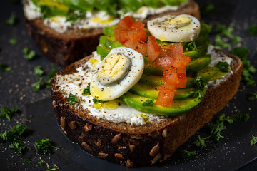 Avocado sandwich on dark rye bread made with fresh sliced avocado, chopped tomatoes, eggs, cream...