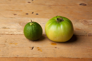 Naranja verde y tomate verde sobre madera
