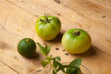 Productos verdes del campo, la hierba de la menta, el tomate verde y la naranja verde sobre una madera rústica.