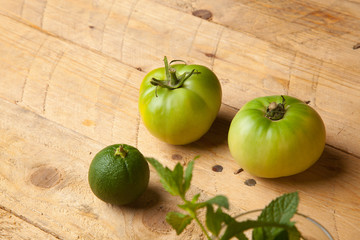Productos verdes del campo, la hierba de la menta, el tomate verde y la naranja verde sobre una madera rústica.