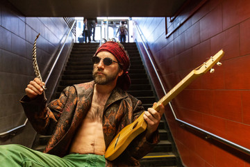Shaman holds guitar in underground. A confident shirtless spiritual man is seen close-up, sitting...
