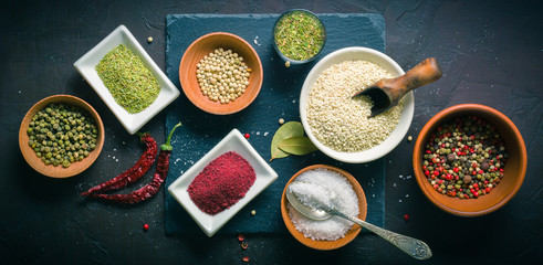 A lot of spices and seasonings in drinking bowls on a dark table. View from above.