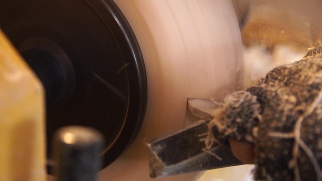 Woodworker handles wood by bench. Making beautiful wooden handmade dish. Craftsman works with workpiece in workshop. Creation of unusual platter. Carpenter cuts wood by graver in soft focus.