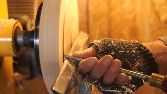 Carpenter handles wood by machine. Builder works with workpiece in workspace. Making beautiful wooden handmade plate. Production of wooden trencher. Woodworker cuts wood by gouge in soft focus.