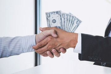 Bribery and corruption concept, bribe in the form of dollar bills, Businessman shaking hands and giving hides money while making deal to agreement a contract