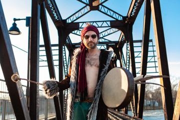 Shirtless boho stands on railroad bridge. A young Caucasian man is seen from the front, with an...