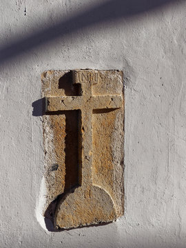 A Carved Stone Cross embedded into the Walls of a House in a street of the Portuguese Town of Estoi on the Algarve on a hot Summers afternoon. Portugal
