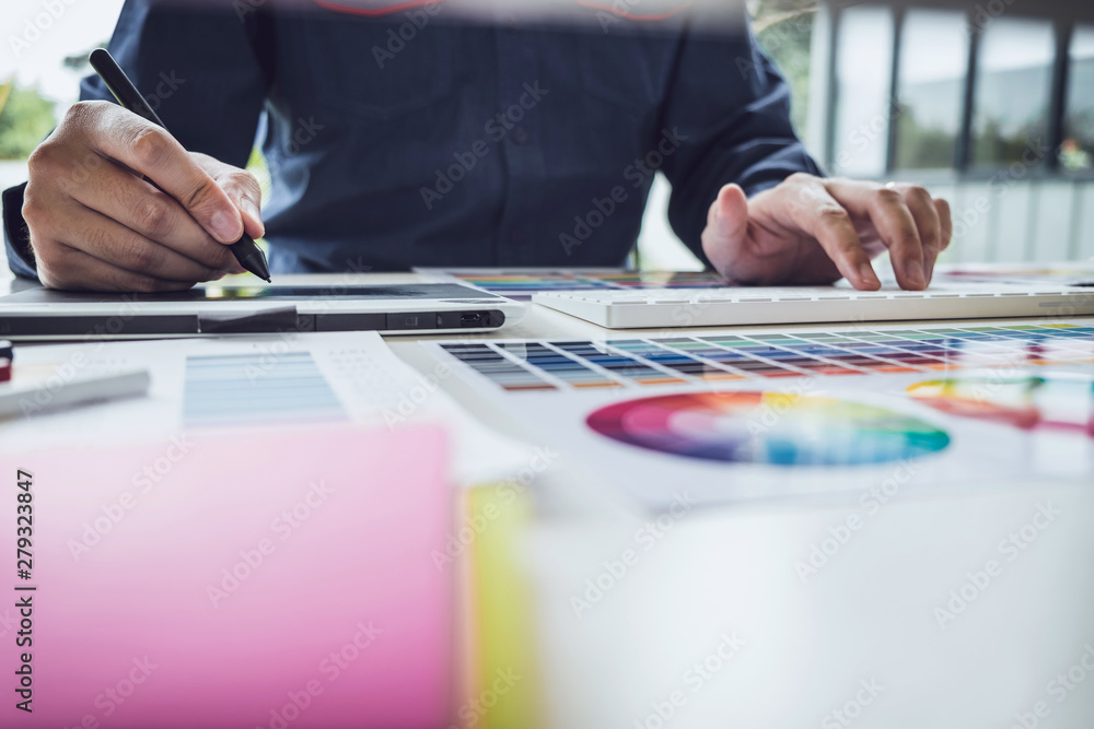 Poster Image of male creative graphic designer working on color selection and drawing on graphics tablet at workplace with work tools and accessories