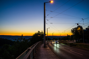 Germany, Cars driving on a road through city stuttgart in magical dawning twilight after sunset near eugensplatz next to rails of tram in summer
