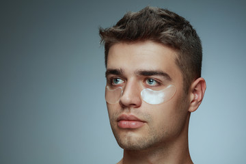Naklejka premium Close-up profile portrait of young man isolated on grey studio background. Male face with collagen patches under eyes. Concept of men's health and beauty, cosmetology, body and skin care. Anti-aging.
