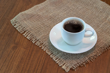 Hot coffee in white cup on sack and teak wood table