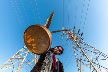 Sacred man beneath electricity towers. A worm's eye shot of a medicine man holding a sacred drum...