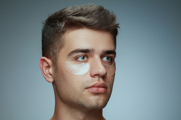 Fototapeta premium Close-up profile portrait of young man isolated on grey studio background. Male face with collagen patches under eyes. Concept of men's health and beauty, cosmetology, body and skin care. Anti-aging.
