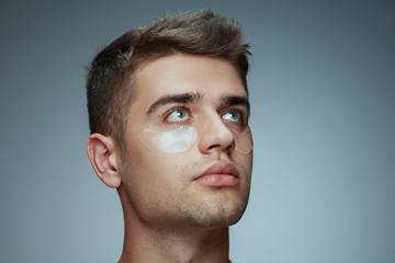 Fototapeta premium Close-up profile portrait of young man isolated on grey studio background. Male face with collagen patches under eyes. Concept of men's health and beauty, cosmetology, body and skin care. Anti-aging.