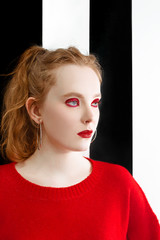 portrait of beautiful young redhead girl with stylish make up and in red sweater on black and white background