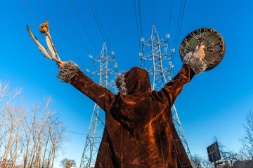 Sacred man beneath electricity towers. A spiritual guy is viewed from behind as he raises a native...