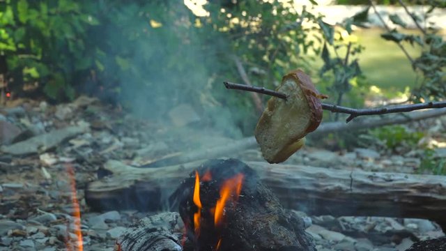 A piece of bread is fried on a stick over a fire in a forest by the river. concept - vacation.