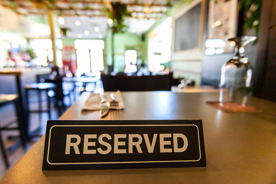 Reserved sign on restaurant table. A table reservation sign is viewed close up inside a trendy bistro, place settings and decor are blurred out in the background with copy space to the top.