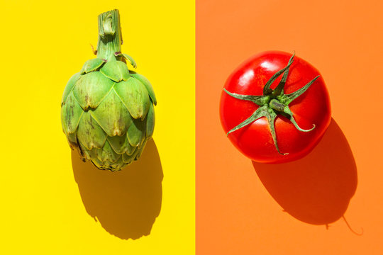 Ripe green artichoke red tomato on duotone yellow orange background with hard light harsh shadows. Trendy funky creative style for food poster banner of Mediterranean cuisine vegan concept