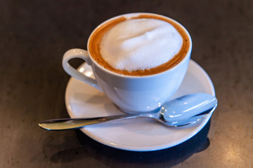 Freshly brewed coffee in coffeehouse. A close-up shot of a just served frothy cappuccino on a table inside a coffee shop, hot morning drink prepared in a white porcelain cup and saucer.