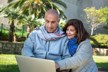 Fototapeta premium coppia matura guarda felice il proprio computer portatile in un parco