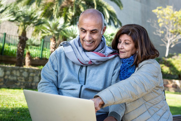 coppia matura guarda felice il proprio computer portatile in un parco
