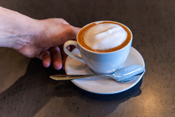 Freshly brewed coffee in coffeehouse. A closeup view on a person's hand reaching for a freshly prepared latte in a coffeeshop. Aromatic breakfast drink served in establishment.