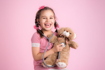 Happy Child Girl Doctor Examining Her Dear Toy Bear on Pink Background