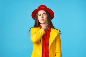 a woman with closed eyes in a red hat holding her neck against a blue background