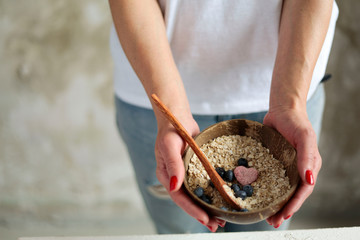 holding cereal and berries in coconut bowl close up. healthy and diet nutrition. 