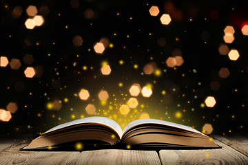 open magic book on a wooden table with glitter and bokeh lights, and black background  with copy space for your text