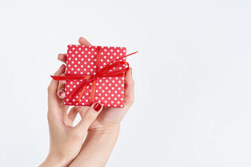 woman hands holding red gift with ribbon, manicured hands with nail polish on white background with copy space