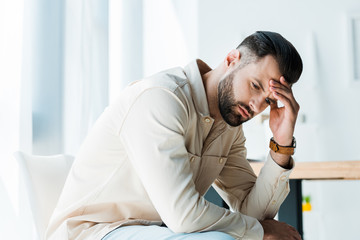 Obraz premium handsome upset man sitting and touching head in office