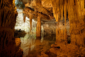 Imposing stalactites and stalacmites reflecting in a small underground lake inside the limestone...