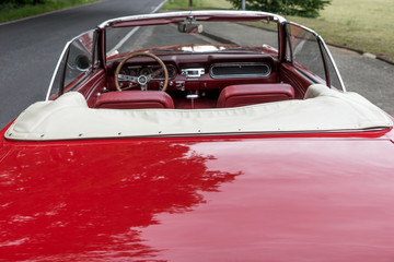 Red old cabriolet is parked at the roadside