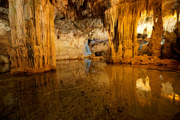 Imposing stalactites and stalacmites reflecting in a small underground lake inside the limestone...