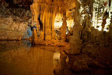 Imposing stalactites and stalacmites reflecting in a small underground lake inside the limestone...