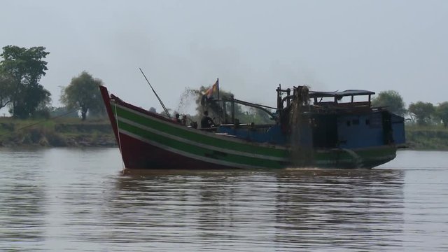 A daylight medium shot of a motor-powered pump boat carrying local passengers while passing through the murky waters of the river.