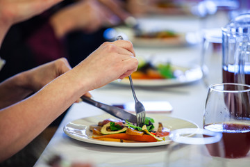 Fototapeta na wymiar Food served at a conference lunch break. A close up and side view of a woman's hands using a knife and fork to eat a freshly prepared avocado salad during a conference lunch in formal setting.
