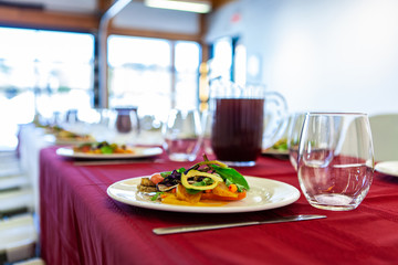 Food served at a conference lunch break. Vegetarian salads are seen close up, served on ceramic dishes inside a workplace conference room, large windows provide airy atmosphere.