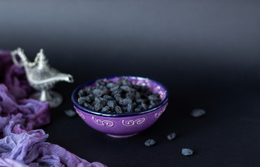A handful of raisins in the purple plate with purple and black wooden background. Eastern sweets....