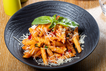 Pasta penne Napoli, traditional italian cuisine dish, chili, tomato and parmesan sauce, in a white or black plate, restaurant setting