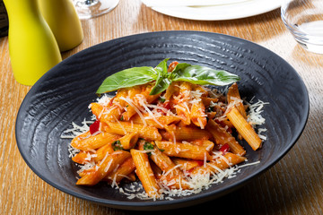 Pasta penne Napoli, traditional italian cuisine dish, chili, tomato and parmesan sauce, in a white or black plate, restaurant setting