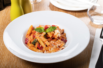 Pasta penne Napoli, traditional italian cuisine dish, chili, tomato and parmesan sauce, in a white or black plate, restaurant setting