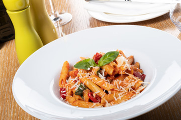 Pasta penne Napoli, traditional italian cuisine dish, chili, tomato and parmesan sauce, in a white or black plate, restaurant setting
